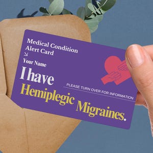 May include: A purple medical alert card with the text "I have Hemiplegic Migraines." The card also includes the text "Medical Condition Alert Card" and a graphic of hands forming a heart. The card is partially inside a brown envelope.