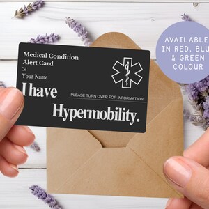 May include: A black medical alert card with white text and a medical symbol is held in front of a brown envelope. The card reads "Medical Condition Alert Card" and "I have Hypermobility." Available in red, blue, and green.