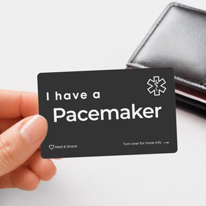 May include: A rectangular black medical alert card with white text that reads I have a Pacemaker. The card features a white Star of Life symbol in the top right corner, a small heart icon with the text Med & Grace, and Turn over for more info.