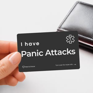 May include: A rectangular black medical alert card with white text that reads I have Panic Attacks. The card features a white Star of Life symbol in the top right corner, a small heart icon with the text Med & Grace, and Turn over for more info.