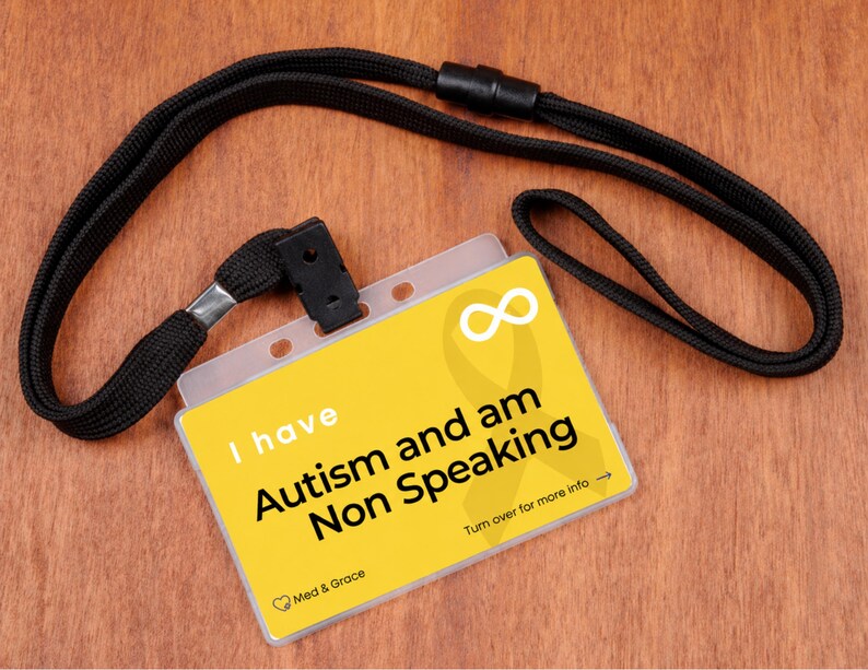 May include: A yellow rectangular identification card attached to a black fabric lanyard. The card features a white infinity symbol, a yellow ribbon graphic, and the black text: I have Autism and am Non Speaking. Turn over for more info.