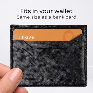 May include: A black textured card holder with a rectangular orange card inserted. The card features the white text "I have" on the left side. Above the card holder, the text reads "Fits in your wallet" and "Same size as a bank card."