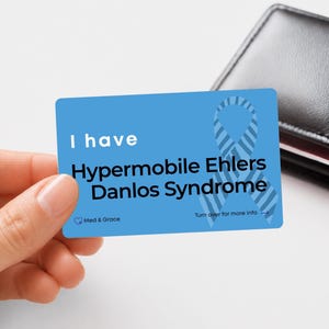 May include: A rectangular blue medical alert card featuring a light blue striped awareness ribbon. The text reads: I have Hypermobile Ehlers Danlos Syndrome, Med & Grace, and Turn over for more info with an arrow pointing to the right side.