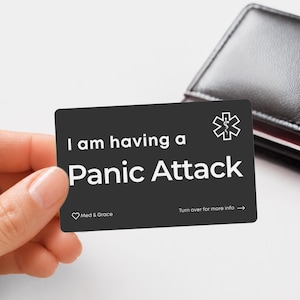 May include: A rectangular black medical alert card with white text that reads I am having a Panic Attack, featuring a white Star of Life symbol, the text Med & Grace with a heart icon, and the instruction Turn over for more info with an arrow.