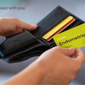 May include: A black leather wallet containing a yellow card with the text I have Endometriosis and a yellow ribbon graphic. The card also features the text Turn over for more info and the text Always with you is visible in the upper left corner.