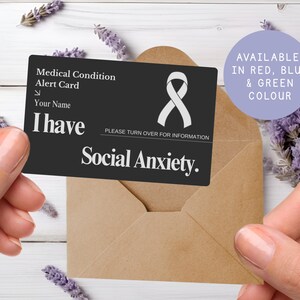May include: A black medical alert card with white text and a white ribbon symbol, held in front of a brown envelope. The card reads "I have Social Anxiety." A purple circle states "Available in Red, Blue & Green Colour."