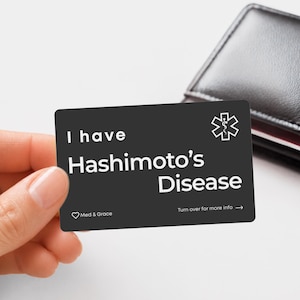 May include: A rectangular black medical alert card with white text that reads I have Hashimoto's Disease. The card features a white medical symbol in the top right corner, a small heart icon with the text Med & Grace, and Turn over for more info.
