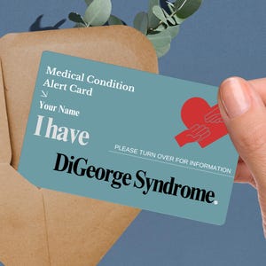May include: A blue medical alert card with a red heart and hands holding it. The card says "Medical Condition Alert Card" and "I have DiGeorge Syndrome."