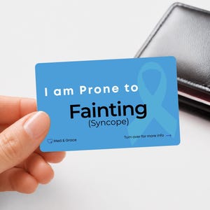 Peut inclure: Une carte d'alerte médicale rectangulaire bleue avec un ruban de sensibilisation bleu clair et le texte blanc et noir : I am Prone to Fainting (Syncope). La carte inclut le logo Med & Grace et le texte Turn over for more info avec une flèche.