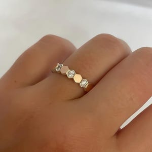 Può includere: Un anello d'oro con una fila di pietre esagonali incastonate con piccoli diamanti trasparenti.