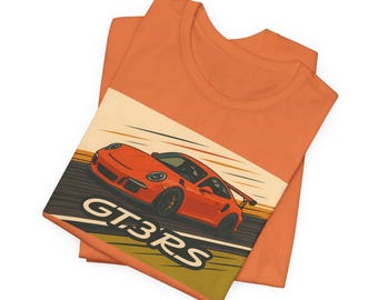 Puede incluir: Camiseta naranja con un gráfico de un Porsche GT3RS rojo en un circuito de carreras amarillo y marrón. El texto "GT3RS" está impreso en la camiseta.
