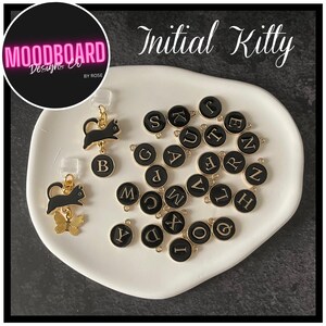 May include: A collection of Initial Kitty charms and earrings. The charms are black with gold trim and feature letters of the alphabet. The earrings have a black cat design with a gold butterfly charm. The image also includes the text "Initial Kitty" and "Moodboard Designs by Rose."