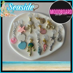 May include: A collection of seashell-themed earrings in various colors and designs, including starfish, scallop shells, and seahorses. The earrings are displayed on a white surface, with the word "Seaside" in the upper left corner.