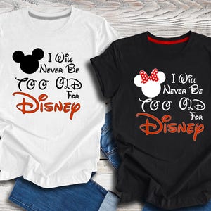 Puede incluir: Dos camisetas con un Mickey Mouse blanco y negro y un Minnie Mouse rojo y blanco. El texto en las camisetas dice "I Will Never Be Too Old For Disney".