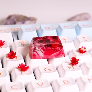 May include: A red and white resin keycap with a swirl pattern sits on a white keyboard. The keycap is on the 'G' key.