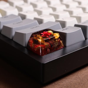 Peut inclure: Gros plan d'un capuchon de touche en résine rouge, jaune et marron avec un motif floral. Le capuchon de touche est posé sur un clavier noir.