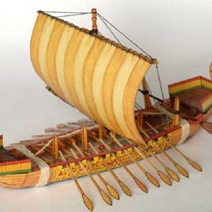 Pode incluir: Um modelo detalhado de uma galera romana antiga com uma vela listrada, remos e esculturas intrincadas. O barco é feito de madeira e pintado em tons de marrom, amarelo e vermelho.