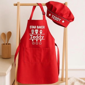 May include: A red apron and chef's hat set. The apron features the words "STAR BAKER" and "TEDDY" in white, with baking icons and stars. The chef's hat is red and has the name "TEDDY" and stars. A fun gift for a young baker.