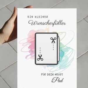 May include: A white rectangular greeting card featuring the text "EIN KLEINER Wunscherf&uuml;ller F&Uuml;R DEIN NEUES iPad" in black. The center displays a tablet illustration with a stylus and two scissor icons connected by dashed lines over watercolor splashes.
