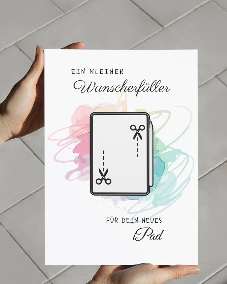 May include: A white rectangular greeting card featuring the text "EIN KLEINER Wunscherf&uuml;ller F&Uuml;R DEIN NEUES iPad" in black. The center displays a tablet illustration with a stylus and two scissor icons connected by dashed lines over watercolor splashes.
