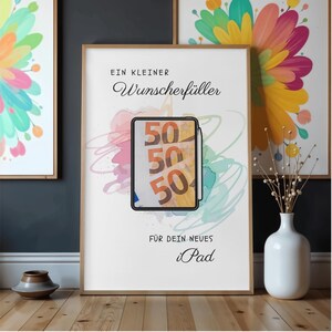 May include: A framed poster featuring the German text "EIN KLEINER Wunscherf&uuml;ller" at the top and "F&Uuml;R DEIN NEUES iPad" at the bottom. The center displays a tablet illustration showing three fifty-euro banknotes with a stylus attached to the side.