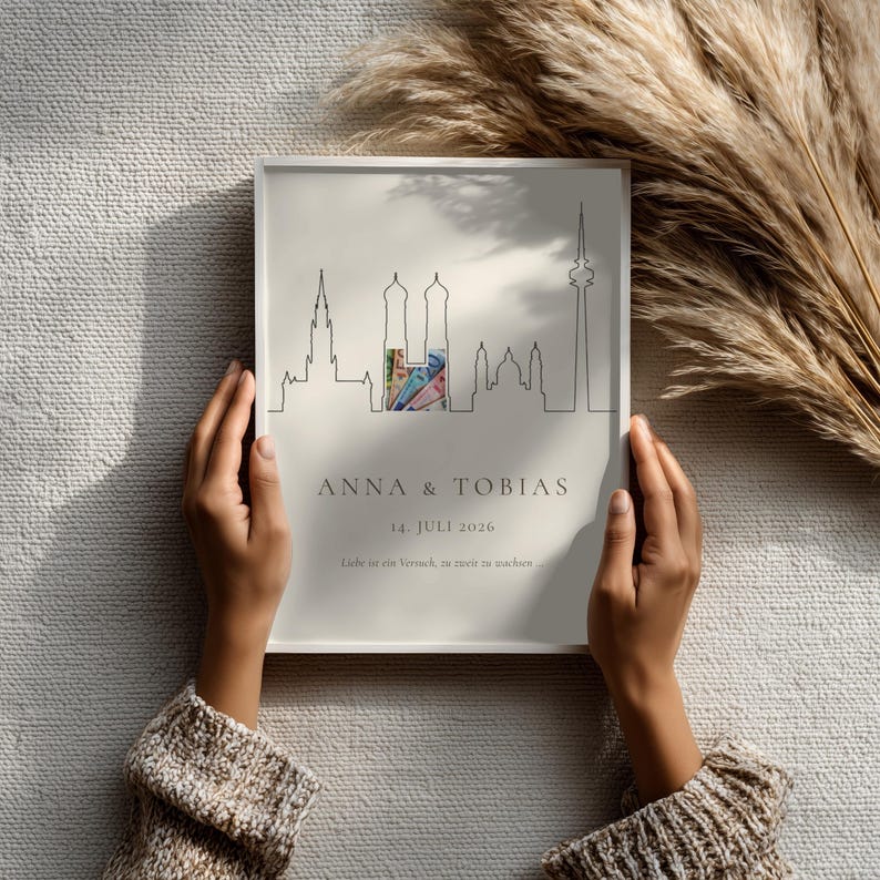 K&ouml;nnte beinhalten: Gerahmter Druck mit minimalistischem Skyline-Design, den Namen "ANNA & TOBIAS" und dem Datum "14. JULI 2026". Das Kunstwerk enth&auml;lt einen farbigen Abschnitt innerhalb der Skyline.