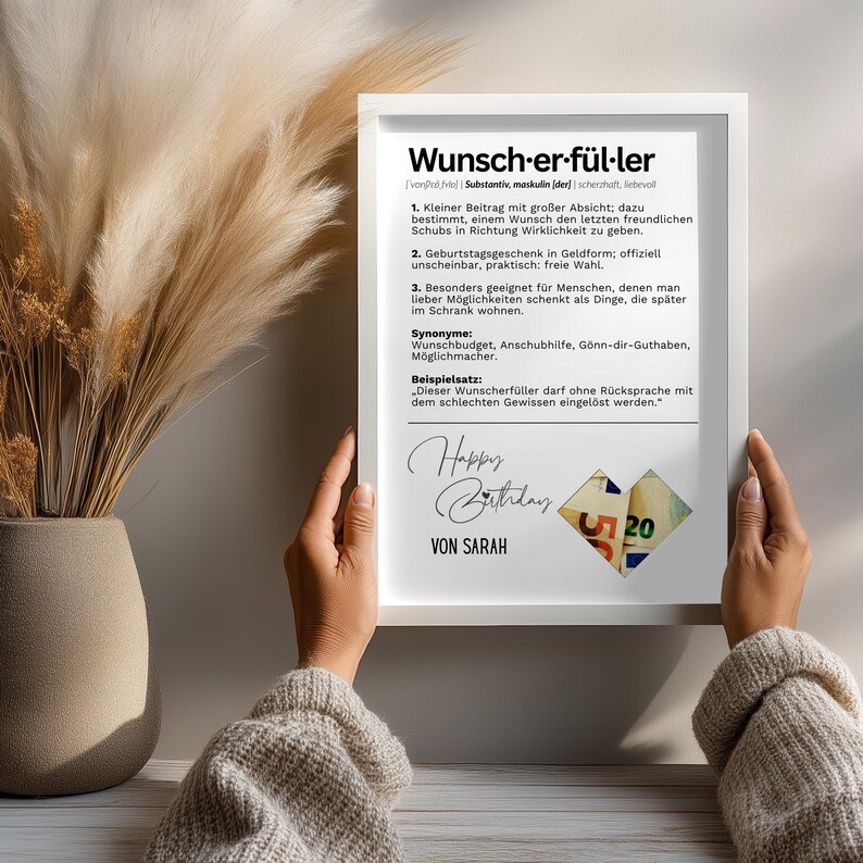 May include: A framed print with the German word "Wunscherf&uuml;ller" and its definition. The print includes the text "Happy Birthday" and "Von Sarah". The image is held by a person.