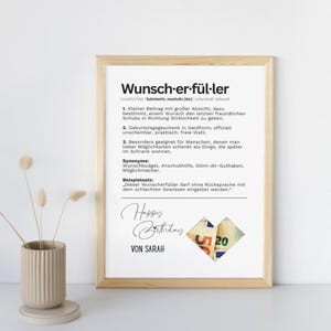 May include: A framed print with the German word "Wunscherf&uuml;ller" and its definition. The print includes the text "Happy Birthday" and "Von Sarah", with a collage of money. The frame is a light brown color.