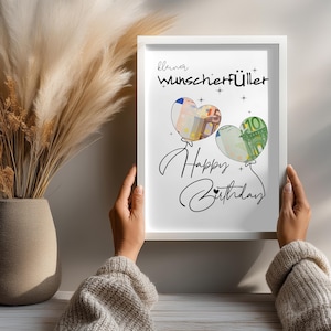 K&ouml;nnte beinhalten: Ein wei&szlig;er Bilderrahmen mit einem Druck, der den Text "kleiner Wunscherf&uuml;ller" und "Happy Birthday" in schwarzer Schrift zeigt. Zwei herzf&ouml;rmige Ballon-Illustrationen enthalten Bilder eines 50- und 100-Euro-Scheins, verziert mit kleinen Sternen.