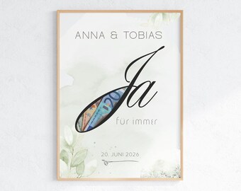 Könnte beinhalten: Ein gerahmter Druck mit dem Text ANNA & TOBIAS, dem Wort Ja und dem Schriftzug für immer. Der Buchstabe J enthält einen Ausschnitt, der Euro-Banknoten zeigt. Darunter steht das Datum 20. JUNI 2026 und eine kleine Ring-Zeichnung. Grüne Blätter.