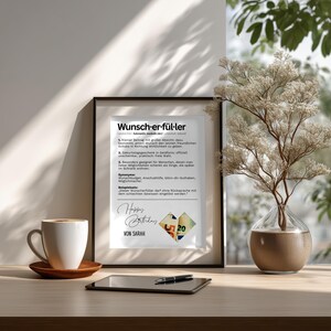 May include: A framed print with the German word "Wunsch-er-f&uuml;ller" and text. The print includes the words "Happy Birthday" and "Von Sarah". A cup of coffee, a tablet, and a vase with branches are on the table.