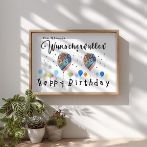 May include: A framed print with the words "Happy Birthday" in black script. Two balloon-shaped images are filled with colorful currency. Colorful balloons float below the text, and the words "Ein kleiner Wunscherf&uuml;ller" are at the top.