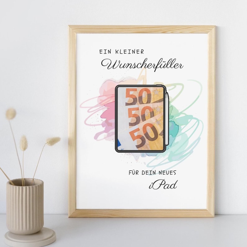 May include: A framed print featuring a light wood frame and white background. The text reads EIN KLEINER Wunscherf&uuml;ller F&Uuml;R DEIN NEUES iPad. In the center, a tablet illustration displays three fifty-euro banknotes with a stylus attached to the side.