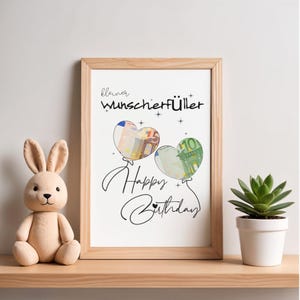 K&ouml;nnte beinhalten: Ein gerahmter Druck mit dem Text "kleiner Wunscherf&uuml;ller" und "Happy Birthday" in schwarzer Schrift. Zwei herzf&ouml;rmige Luftballons sind abgebildet, in deren Inneren Euro-Banknoten zu sehen sind, verziert mit kleinen Sternsymbolen.