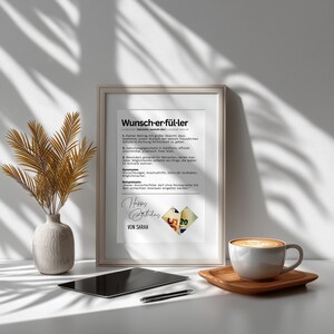 May include: A framed print with the German word "Wunsch-er-f&uuml;l-ler" and text, a vase with dried plants, a tablet, a pen, and a coffee cup on a wooden tray. The print includes the words "Happy Birthday" and "Von Sarah".