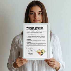 May include: A white framed print with the German word "Wunsch-er-f&uuml;ller" at the top. The print includes text, a heart made of money, and the words "Happy Birthday" and "VON SARAH".