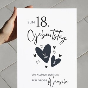 May include: A white rectangular card featuring black text that reads ZUM 18. GEBURTSTAG, followed by two large dark hearts with small scissor icons inside, and the text EIN KLEINER BEITRAG F&Uuml;R GROBE W&uuml;nsche at the bottom with smaller hearts.