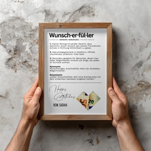 May include: A framed print with the German word "Wunscherf&uuml;ller" at the top, meaning "wish fulfiller". The print includes definitions, synonyms, and a sample sentence. The bottom features "Happy Birthday" and "Von Sarah" with a heart made of money.