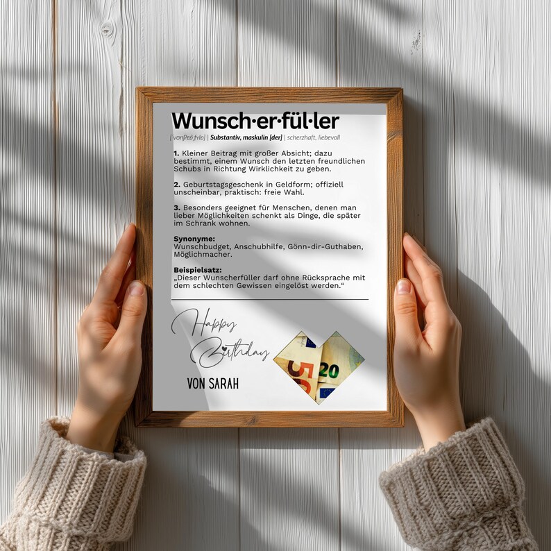 May include: A framed print with German text, including the word "Wunscherf&uuml;ller" and a definition. The print also features the words "Happy Birthday" and "Von Sarah", along with a heart-shaped design with the number 20.