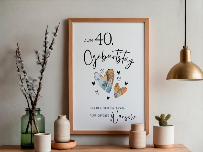 May include: A rectangular wooden frame containing a white print with the text "ZUM 40. GEBURTSTAG" and "EIN KLEINER BEITRAG F&Uuml;R GROBE W&uuml;nsche". The design features two heart-shaped cutouts filled with Euro banknotes, surrounded by small black heart illustrations.