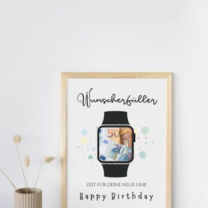 May include: A framed print featuring a black smartwatch illustration with Euro banknotes visible on the screen. The text reads Wunscherf&uuml;ller, ZEIT F&Uuml;R DEINE NEUE UHR, and Happy Birthday, surrounded by small colorful circles on a white background.