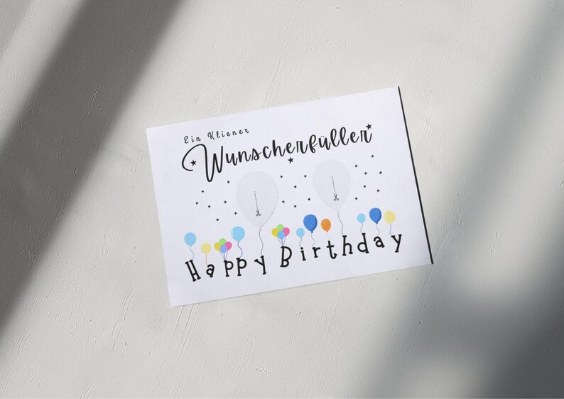 May include: White birthday card with the text "Ein kleiner Wunscherfullen" and "Happy Birthday". The card features illustrations of balloons in various colors, including blue, yellow, and pink.