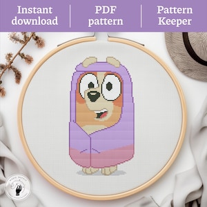 May include: A cross-stitch design of a cartoon dog in a purple hooded outfit, displayed in a wooden embroidery hoop. The image includes the text "Instant download", "PDF pattern", and "Pattern Keeper". The "Magic Needle Cross Stitch Patterns" logo is also visible.