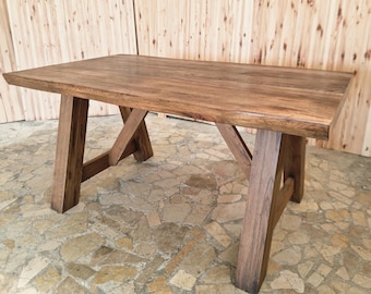 May include: A rectangular wooden table with a natural finish. The table has a solid top and is supported by four sturdy legs with an X-shaped design. The table is made of a light brown wood and is suitable for various uses.