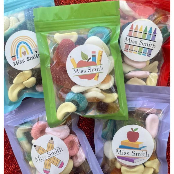 May include: Assorted candies in clear plastic bags with colorful labels. Each bag features a different design, including a rainbow, crayons, pencils, and an apple. The text "Miss Smith" is printed on each label. The bags are sealed and arranged on a red glitter surface.