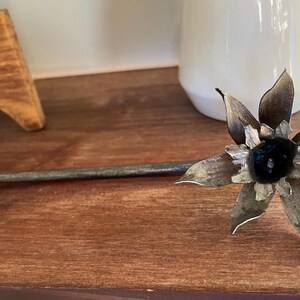 May include: A metal flower with a black center and silver petals on a wooden surface.