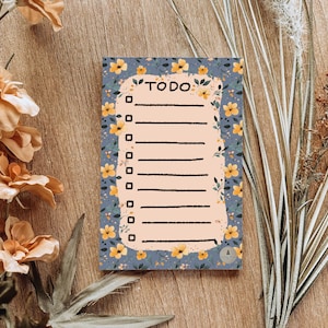 May include: A blue and yellow floral patterned notepad with the word "TO DO" written in black at the top. The notepad has a lined section for writing tasks.