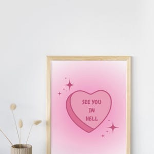 Op de afbeelding: Een ingelijst afdruk met een roze verloopachtergrond. Een roze hartvormige snoepje met de tekst "See you in hell" bevindt zich in het midden van de afdruk. Er zijn kleine witte sterren rond het snoepje. De afdruk is gesigneerd met "M.C."