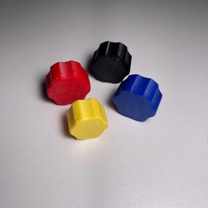 May include: Four plastic knobs in different colors: red, black, blue, and yellow. The knobs have a starburst shape and are arranged in a semi-circle.