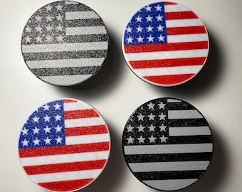 May include: Four round phone grips featuring the American flag design. Two grips have the flag in full color, while the other two are in black and white. The grips are on a white surface.